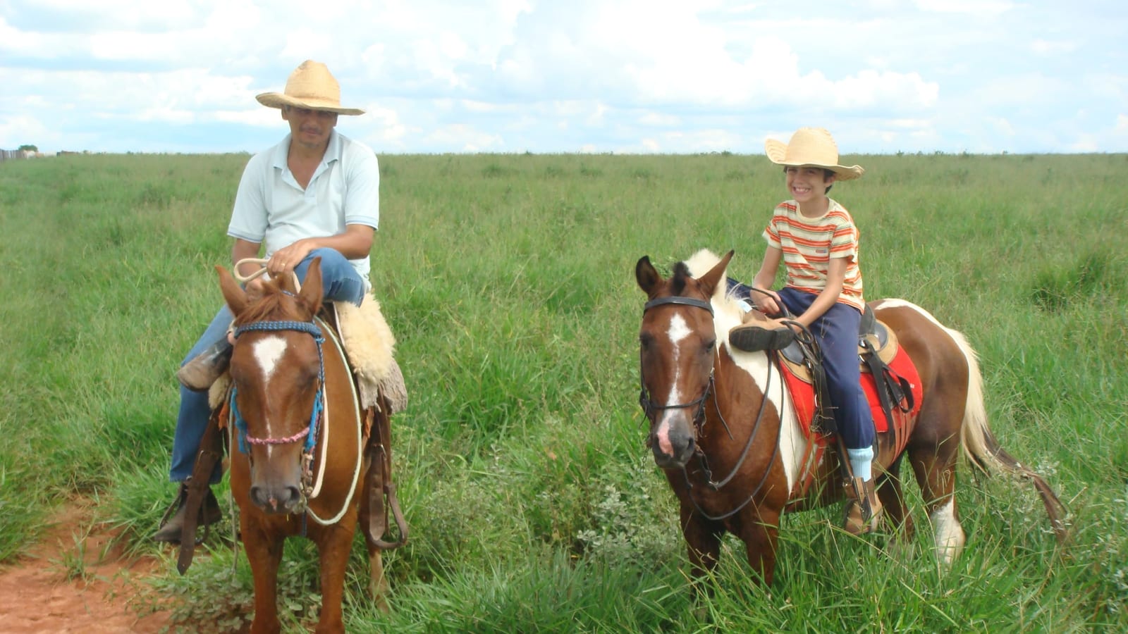 Pedro Henrique criança e o pai, cada um a cavalo, no pasto da fazenda